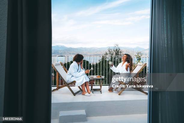 two friends having a good time drinking tea with the scenic view on the balcony - robe stock pictures, royalty-free photos & images