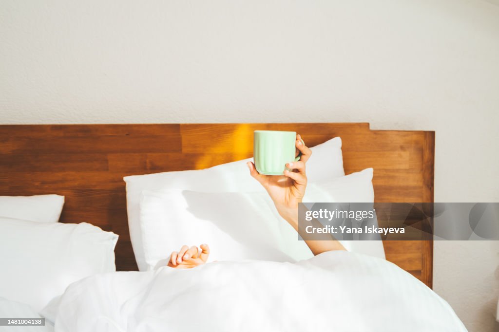 A person having morning coffee in a bed, holding a cup