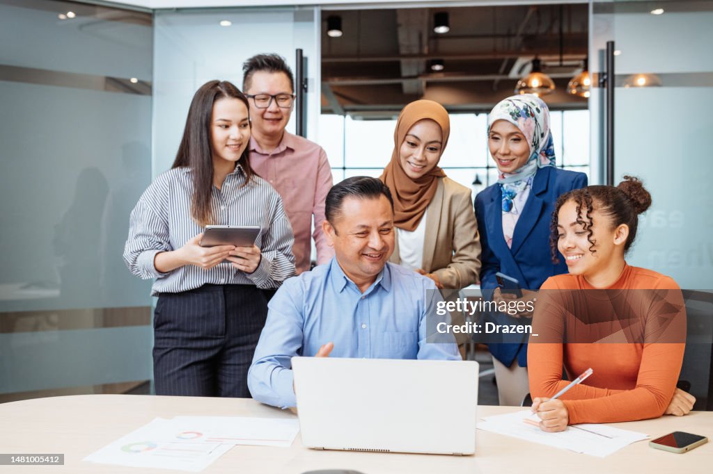 Diverse business people in modern office, looking at laptop and planning investment