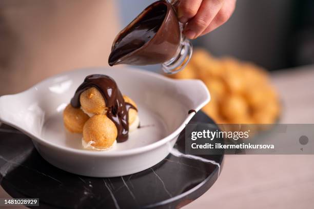 köchin gießt schokoladensoße auf profiterolen - profiterole stock-fotos und bilder