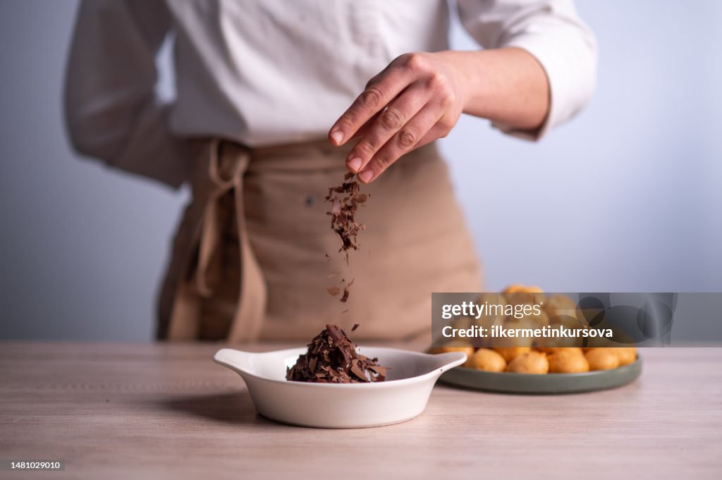 Female chef sprinkling chocolate chip on a bowl of profiteroles with chocolate sauce