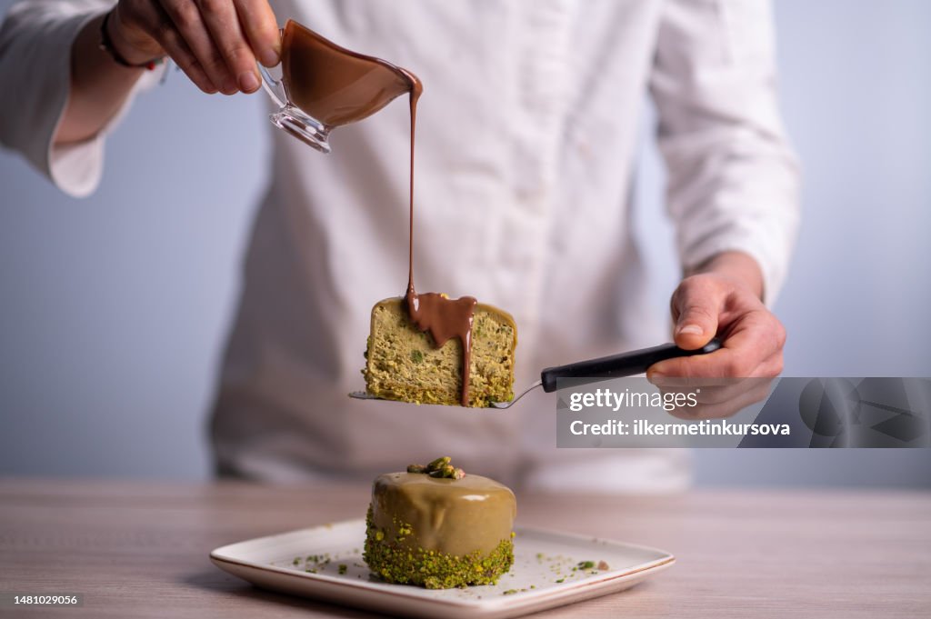 A female chef pouring chocolate sauce on a cake