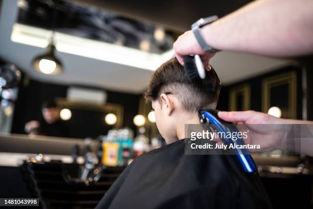 little 7-year-old boy goes to a barbershop to get a modern haircut, rear view shaving - combing stockfoto's en -beelden
