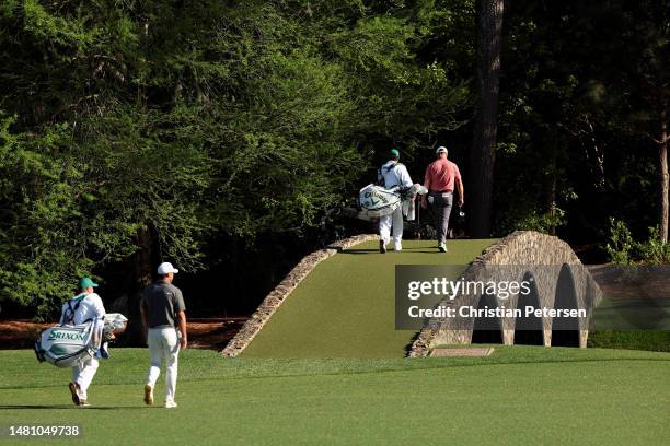 Jon Rahm of Spain and his caddie Adam Hayes cross the Hogan Bridge on the 12th hole as Brooks Koepka of the United States and his caddie Ricky...