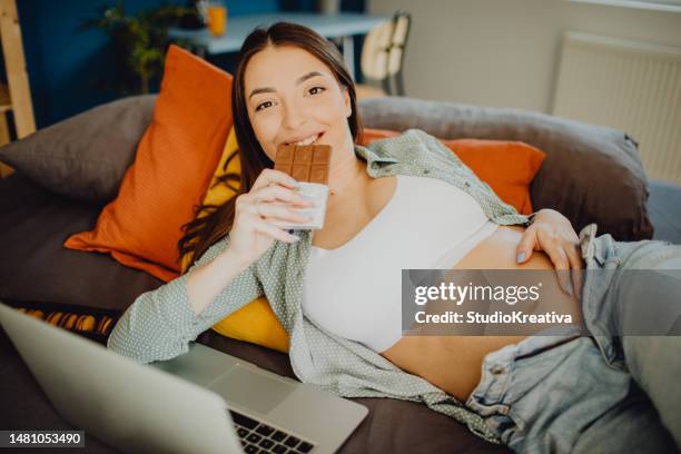 portrait of a pregnant woman eating chocolate while relaxing in her bed - eating dark chocolate stock pictures, royalty-free photos & images