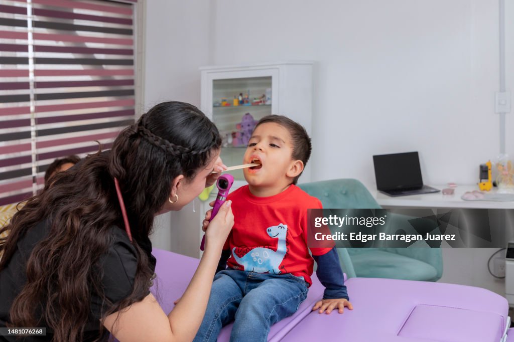A boy opening his mouth while being checked by his doctor with a tongue depressor, with copy space