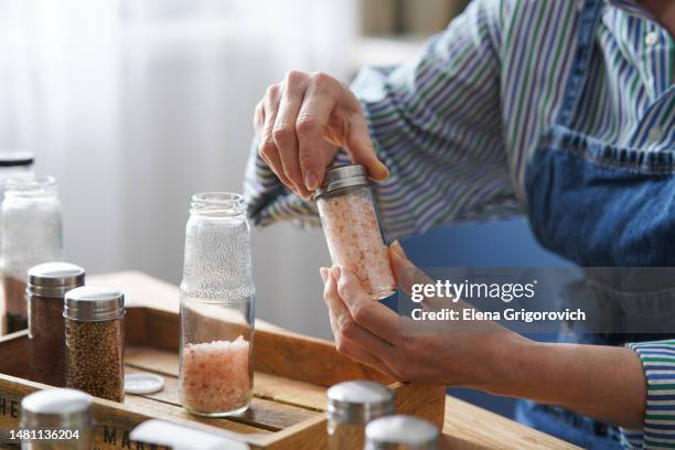 woman's hands holding crushed spices in a glass jar or storage container. process of marking and organize of spices. home staging ideas - spice jar stock pictures, royalty-free photos & images