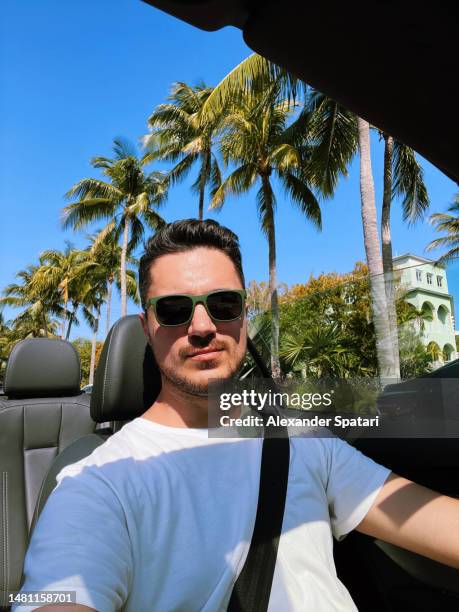 man in sunglasses taking a selfie while driving in a convertible car on a sunny summer day - american influencer stock pictures, royalty-free photos & images