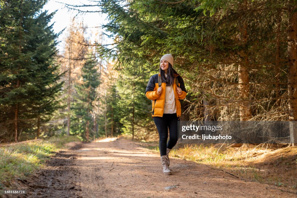 Woman with backpack hiking on footpath in forest at spring