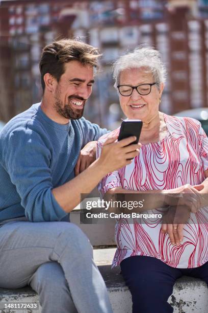 handsome grandson teaches his grandmother how to use smartphone. - pensioners demonstrate in barcelona stock pictures, royalty-free photos & images