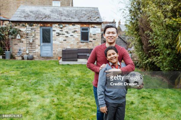 multiethnic asian family at home in uk. step-father playing football with son - child obesity stock pictures, royalty-free photos & images