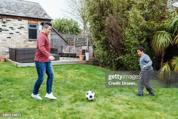 multiethnic asian family at home in uk. step-father playing football with son - child obesity stock pictures, royalty-free photos & images