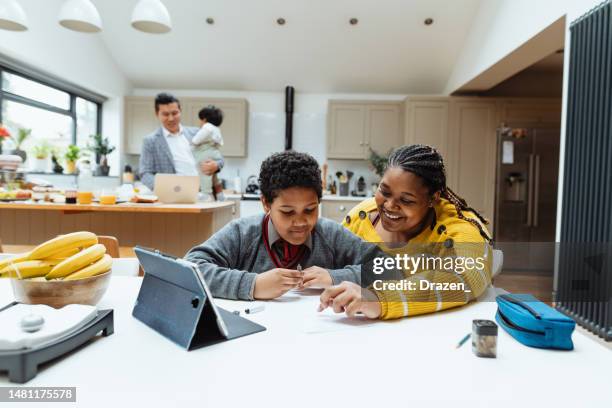 multiethnic asian family at home, mother assisting her son with homework. dad with baby in background. - do my homework stock pictures, royalty-free photos & images