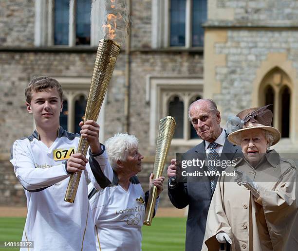 Queen Elizabeth II and Prince Philip, Duke of Edinburgh look on as Olympic torch bearer Gina Macgregor hands the flame to Phil Wells at Windsor...