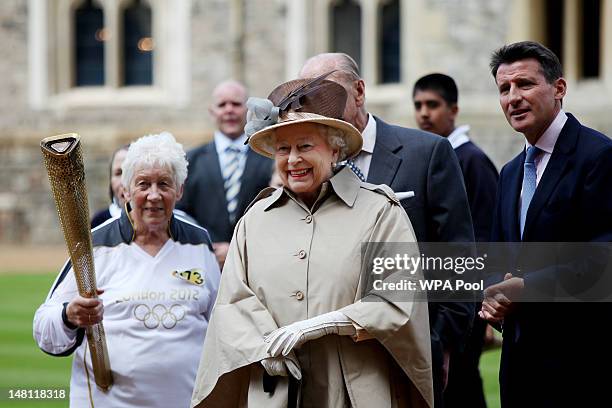 Queen Elizabeth II watches the Olympic torch leave Windsor Castle with the previous torch bearer Gina MacGregor and Sebastian Coe on day 53 of the...