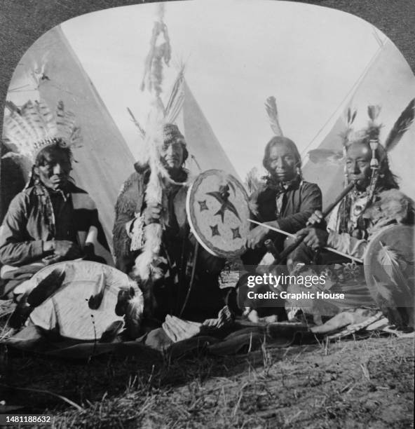 Four Sioux warriors in council, sitting in traditional clothing, with one smoking a peace pipe, United States, circa 1900.