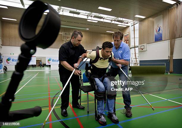 Two men hold Dutch DJ and television presenter Marc de Hond as he tests his exoskeleton in a rehabilitation center in Amsterdam, on July 10, 2012....