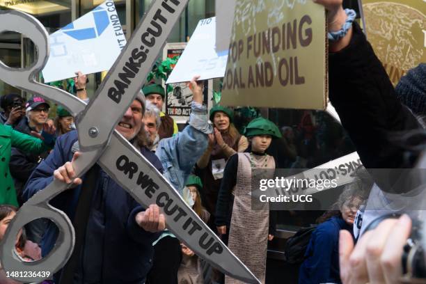 Man displays giant prop scissors used to cut up giant prop credit cards at climate rally and protest outside a JP Morgan Chase and Co office during...