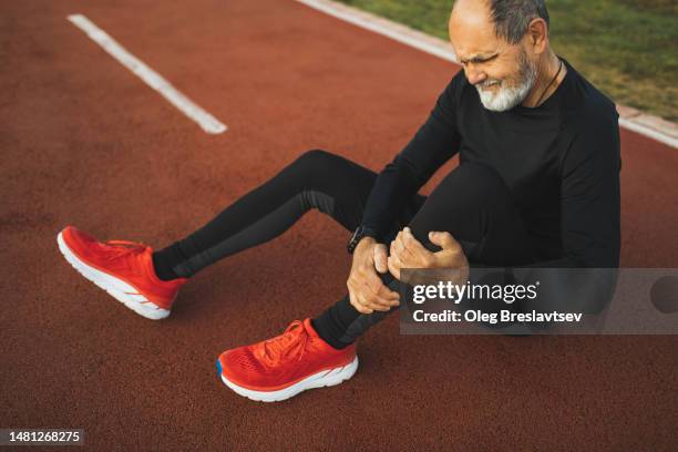 aged man suffering with pain and holding injured leg on running track. health problem - periosteum stock pictures, royalty-free photos & images