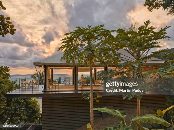 female tourist admiring sea view while sitting on decking of tented villa, illuminated at sunrise with open sides, showing the interior. situated on eco friendly luxury glamping resort. - province de surat thani photos et images de collection