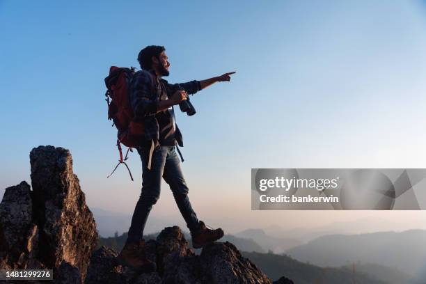 asian backpacker on mountain peak and pointing to sky - aiming higher stock pictures, royalty-free photos & images