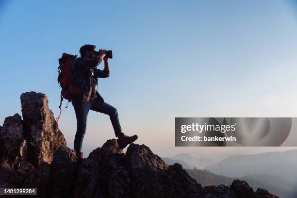 asian backpacker on mountain peak and using binoculars looking forward - verrekijker stockfoto's en -beelden