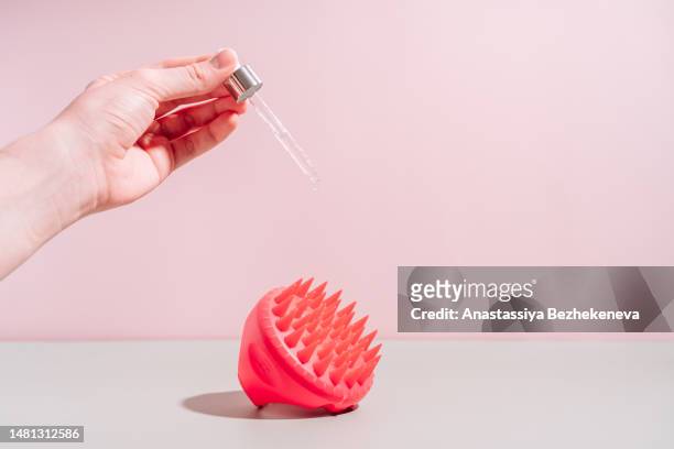 hand pouring serum from pipette onto scalp massager against pink background - cuero cabelludo fotografías e imágenes de stock