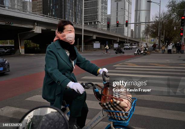 Woman wears a mask and scarf over her face as she rides a shared bike during a sandstorm on April 11, 2023 in Beijing, China. China's capital and the...