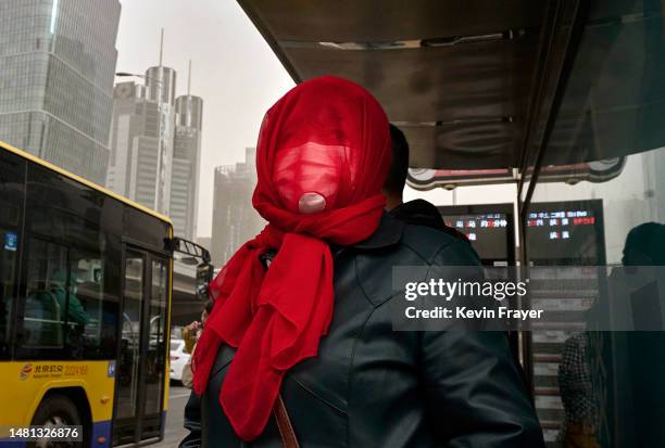 Woman wears a mask and scarf over her face as she waits for a bus during a sandstorm on April 11, 2023 in Beijing, China. China's capital and the...
