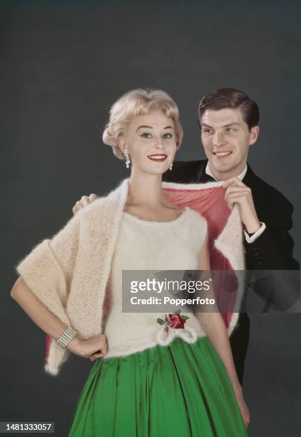 Posed studio portrait of a female fashion model wearing a knitted white mohair wool sleeveless jumper and a green taffeta skirt, the man behind...