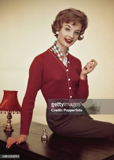Posed studio portrait of a female fashion model wearing a red knitted holiday jacket with contrasting white buttons and top stitching, London, 19th...