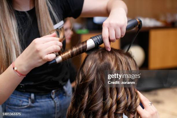 using hot curler and making curls in hair salon - krulspelden stockfoto's en -beelden