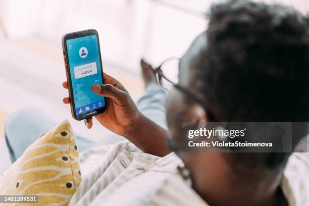 young man using mobile app on smart phone for checking his finances while sitting on the sofa at home. - bank statement bildbanksfoton och bilder