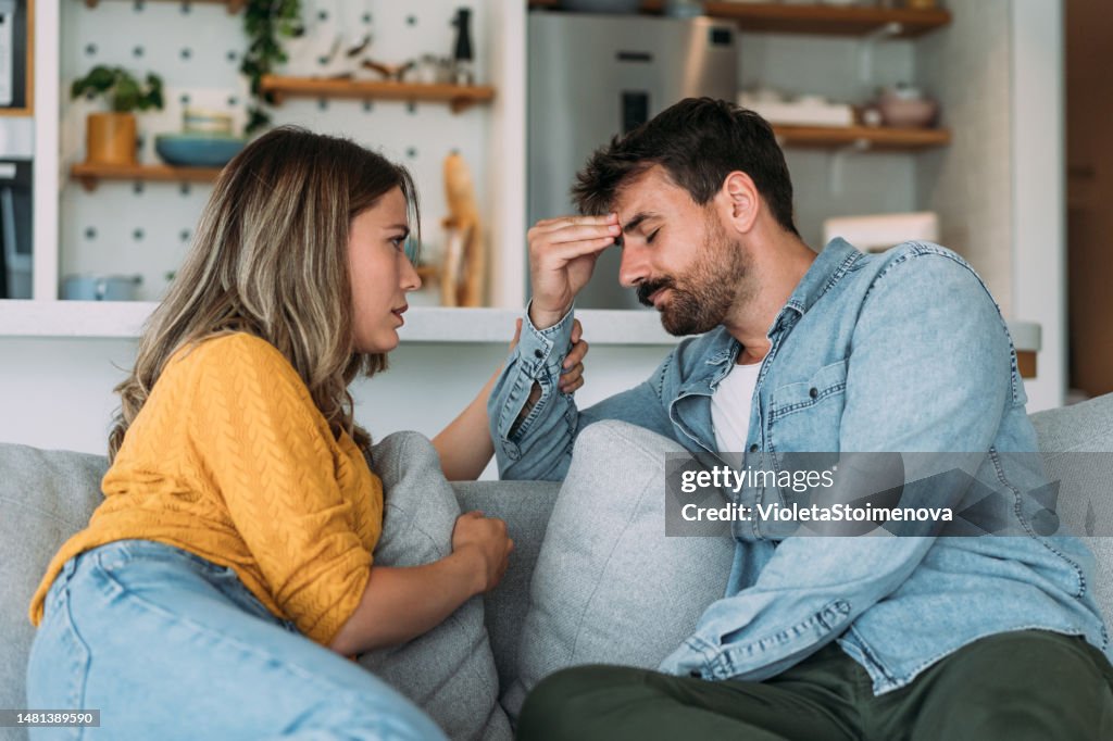 Worried couple talking together in the living room at home.