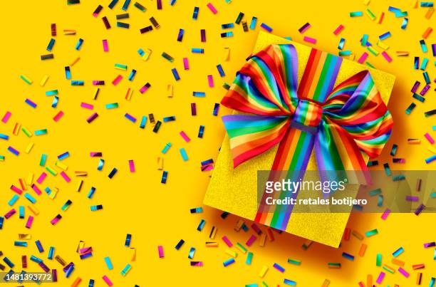 gift box wrapped with a rainbow bow - rainbow confetti stock pictures, royalty-free photos & images