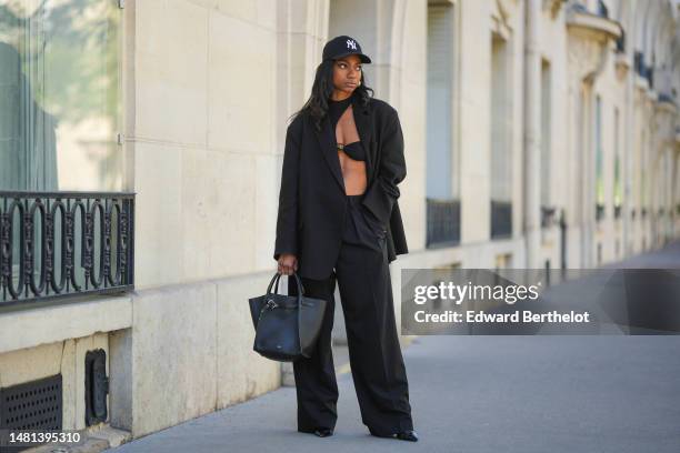 Emilie Joseph wears black sunglasses, gold large earrings, a black cut-out asymmetric shoulder / with a large brown pearl chest bodysuit from...