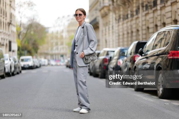 Diane Batoukina wears brown large squared sunglasses from Kaleos, a white t-shirt, a pale gray blazer jacket, matching pale gray large suit pants, a...