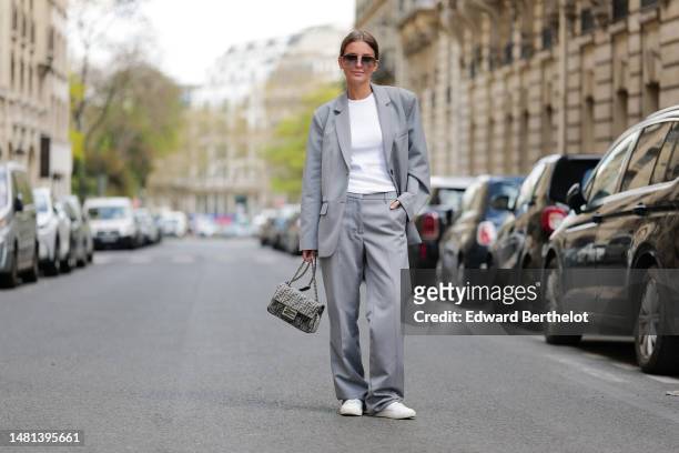 Diane Batoukina wears brown large squared sunglasses from Kaleos, a white t-shirt, a pale gray blazer jacket, matching pale gray large suit pants, a...