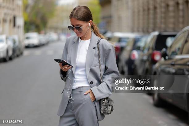 Diane Batoukina wears brown large squared sunglasses from Kaleos, a white t-shirt, a pale gray blazer jacket, matching pale gray large suit pants, a...