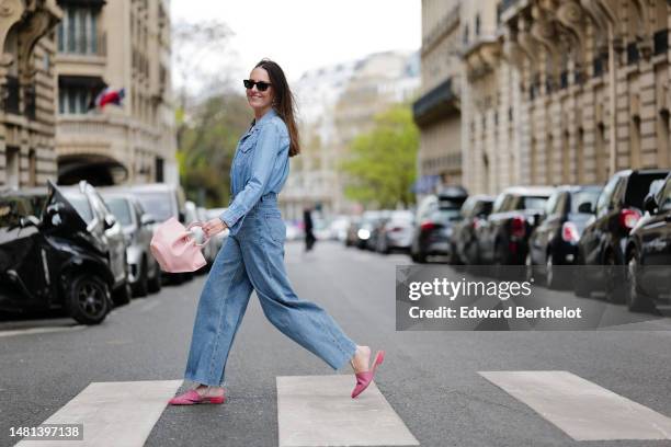 Alba Garavito Torre wears gold large earrings, a white t-shirt, a blue denim buttoned shirt, blue denim wide ripped legs pants, gold bracelets, a...