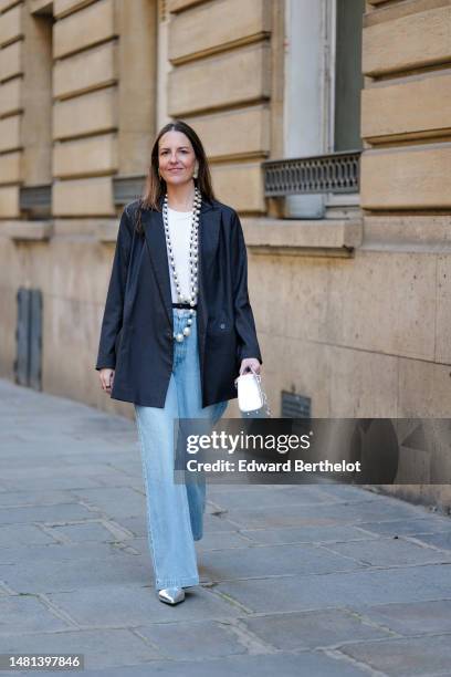 Alba Garavito Torre wears gold earrings, a white large pearls and black small pearls long necklace, a white t-shirt, a dark gray oversized blazer...