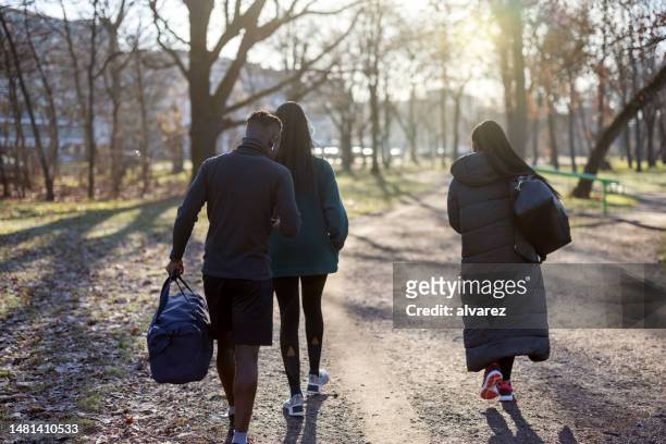 rear view of three young people walking to gym with duffle bags in autumn morning - gymtas stockfoto's en -beelden