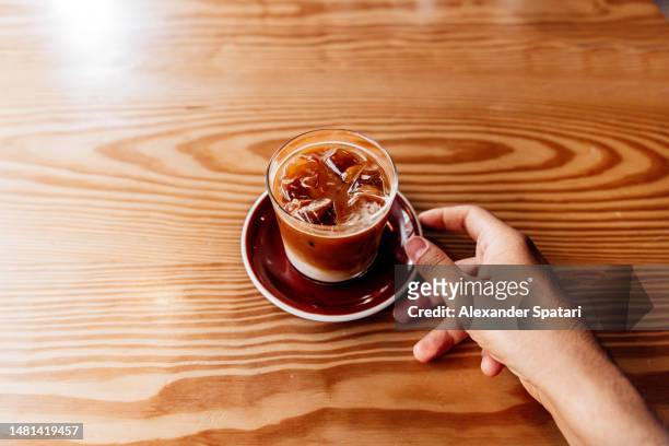 man drinking iced coffee in a coffee shop, personal perspective view - hand resting on wood stock-fotos und bilder