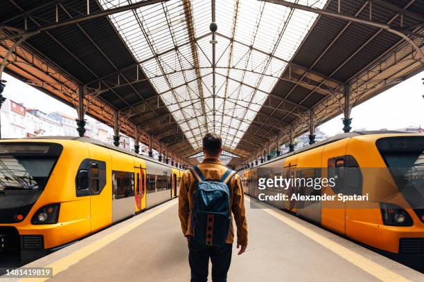 rear view of a man with backpack walking between train on train station - travel stock-fotos und bilder