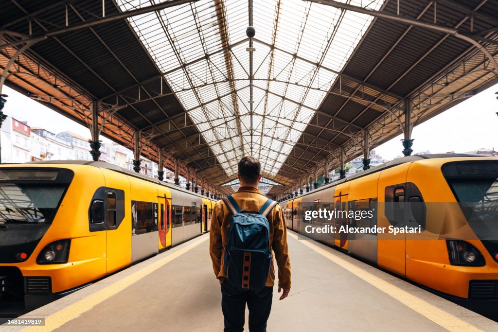 Rear view of a man with backpack walking between train on train station