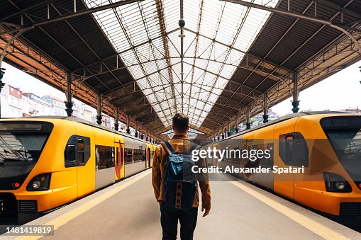Rear view of a man with backpack walking between train on train station Rear view of a man with backpack walking between train on train station