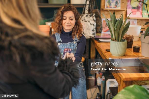 female shop owner taking payment from customer - nailsworth gloucestershire stock pictures, royalty-free photos & images