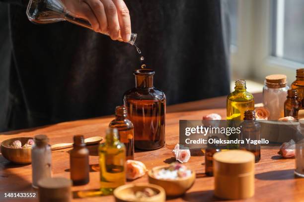 woman preparing aromatic liquid for diffuser on wooden table. many bottles and jars with different types of oils, salt and essences. alternative medicine concept. - perfumería fotografías e imágenes de stock
