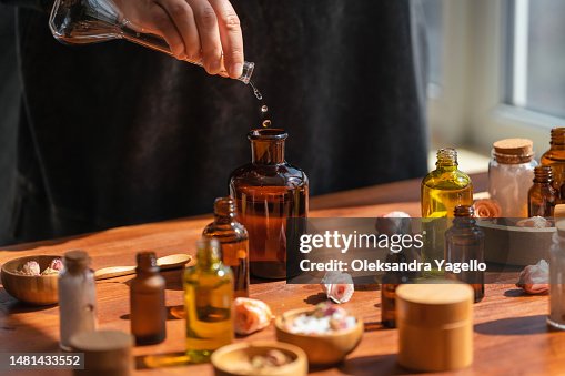 Woman preparing aromatic liquid for diffuser on wooden table. Many bottles and jars with different types of oils, salt and essences. Alternative medicine concept. Woman preparing aromatic liquid for diffuser on wooden table. Many bottles and jars with different types of oils, salt and essences. Alternative medicine concept.