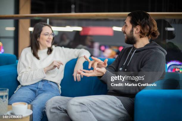 dos jóvenes amigos están sentados en un café y hablando en lenguaje de señas. - american sign language fotografías e imágenes de stock